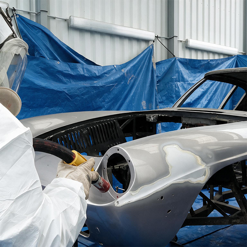 Technicien réalisant l’aérogommage de la carrosserie démontée d’une voiture ancienne dans le cadre d’une restauration complète