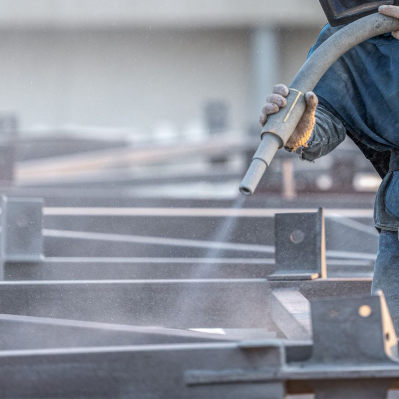 Technicien réalisant l’aérogommage d’une structure métallique en acier dans un atelier pour nettoyer la surface avant finition