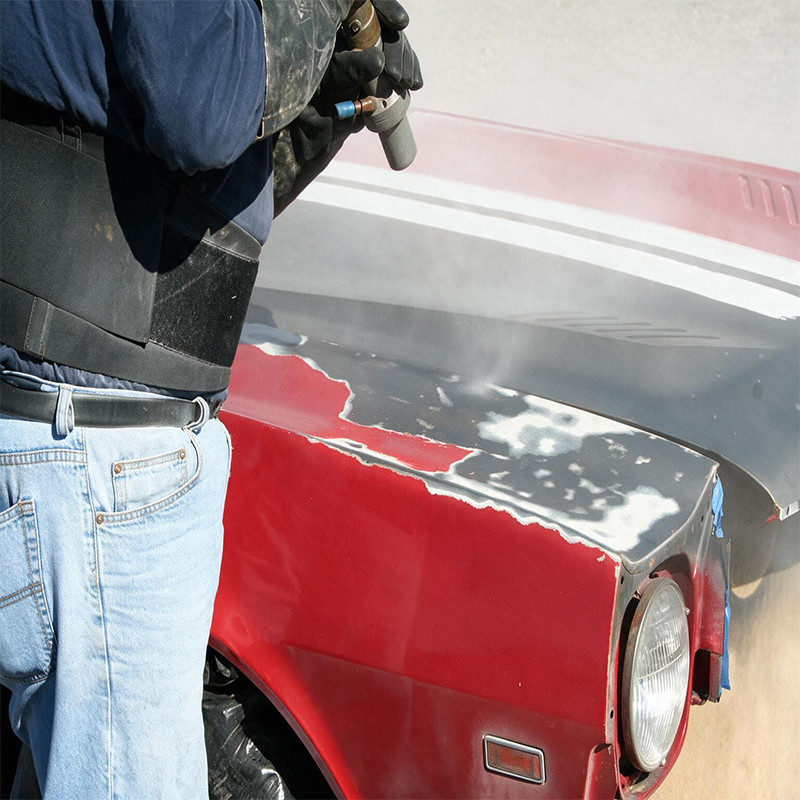 Aérogommage de l’aile avant d’une voiture ancienne rouge pour retirer les anciennes couches de peinture
